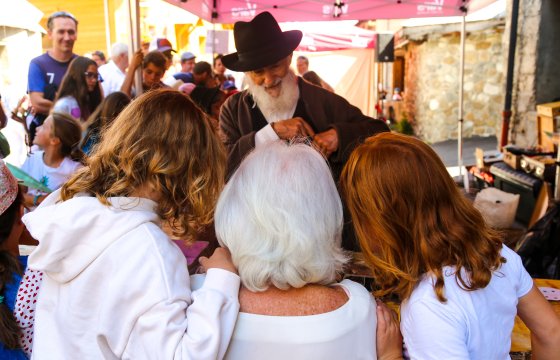 Marché : Stand d'un homme avec un chapeau noir et une barbe blanche, et trois personnes de dos devant
